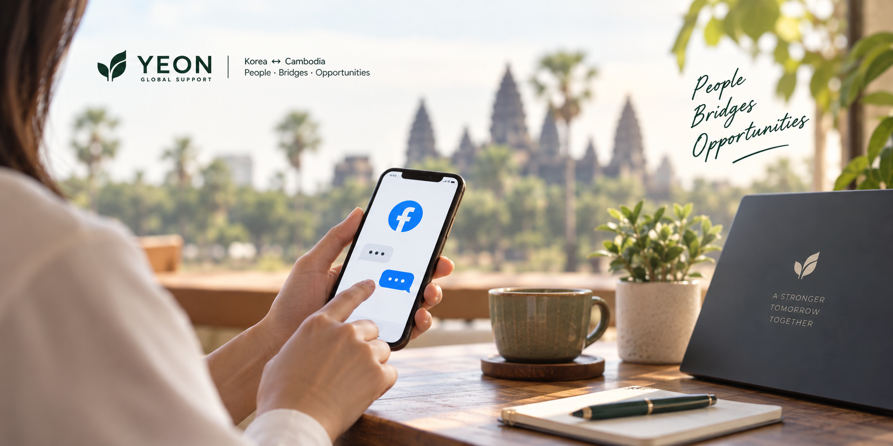 A woman at a café table opens Facebook Messenger on her phone, with Angkor Wat visible through the window behind her.